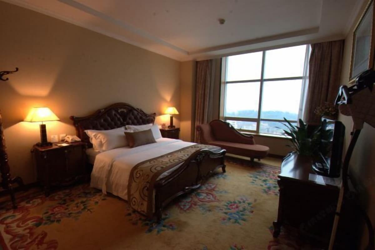 A hotel room with a large bed, two bedside lamps, a chair, a desk, and a window with a view.