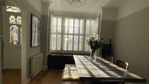 A dining area with a long table, chairs, a vase with flowers, and a hanging light fixture. - A sun-kissed, cozy family home. (London)