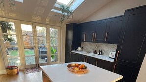 A modern kitchen with dark cabinets, a white countertop, and a built-in dishwasher. There is a skylight above the sink and a view of the backyard through large sliding glass doors. - A sun-kissed, cozy family home. (London)