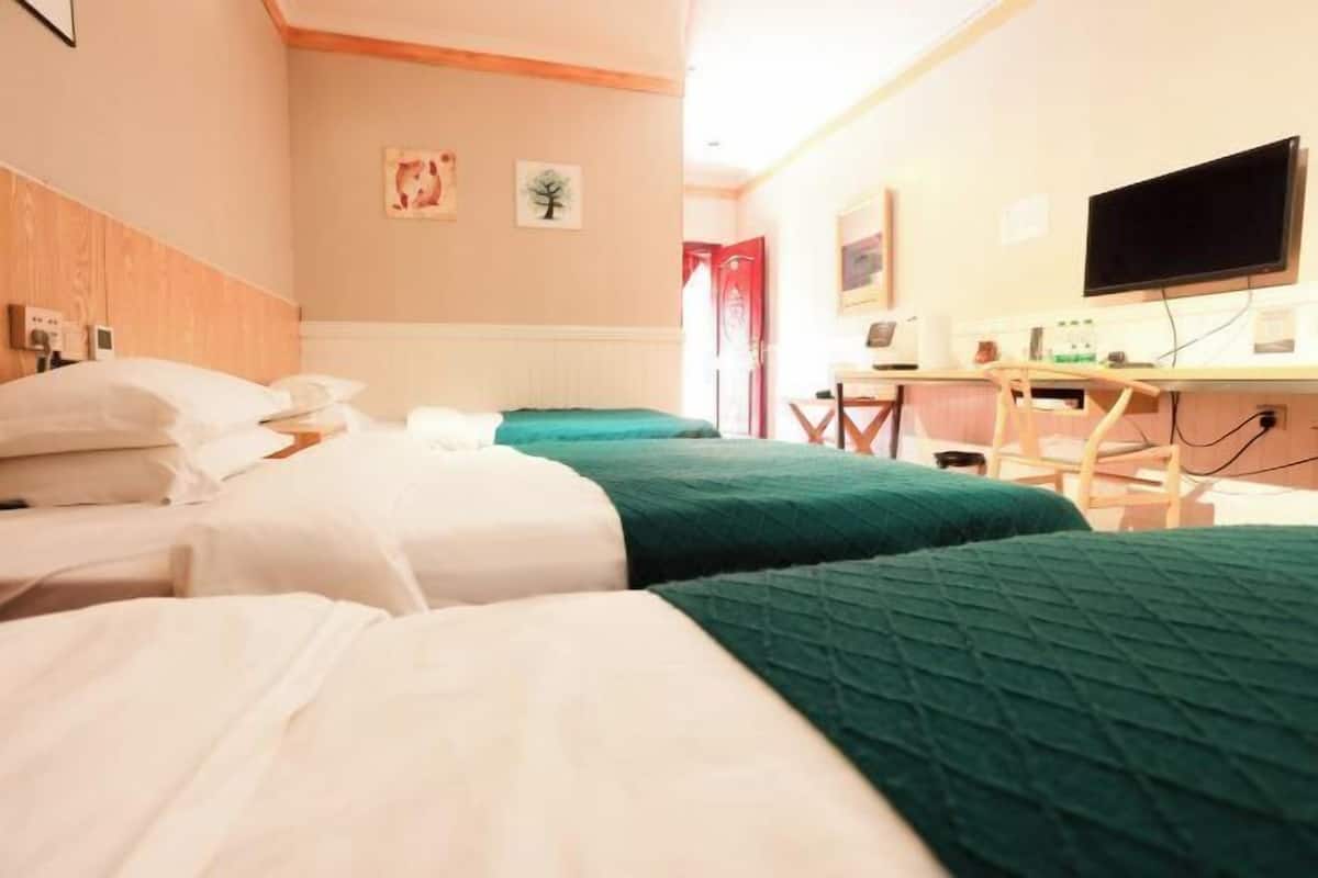 A hotel room with three beds, a desk, a television, and a window.