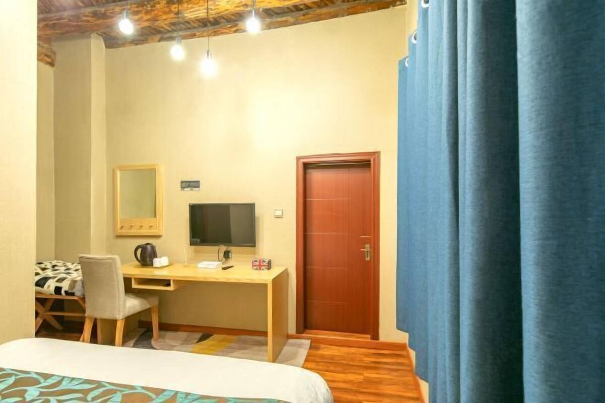 A bedroom with a bed, a desk with a computer, a chair, a mirror, and a door.