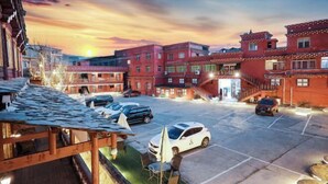 Un patio con cubierta de madera, una zona de estar techada y un estacionamiento con varios coches.