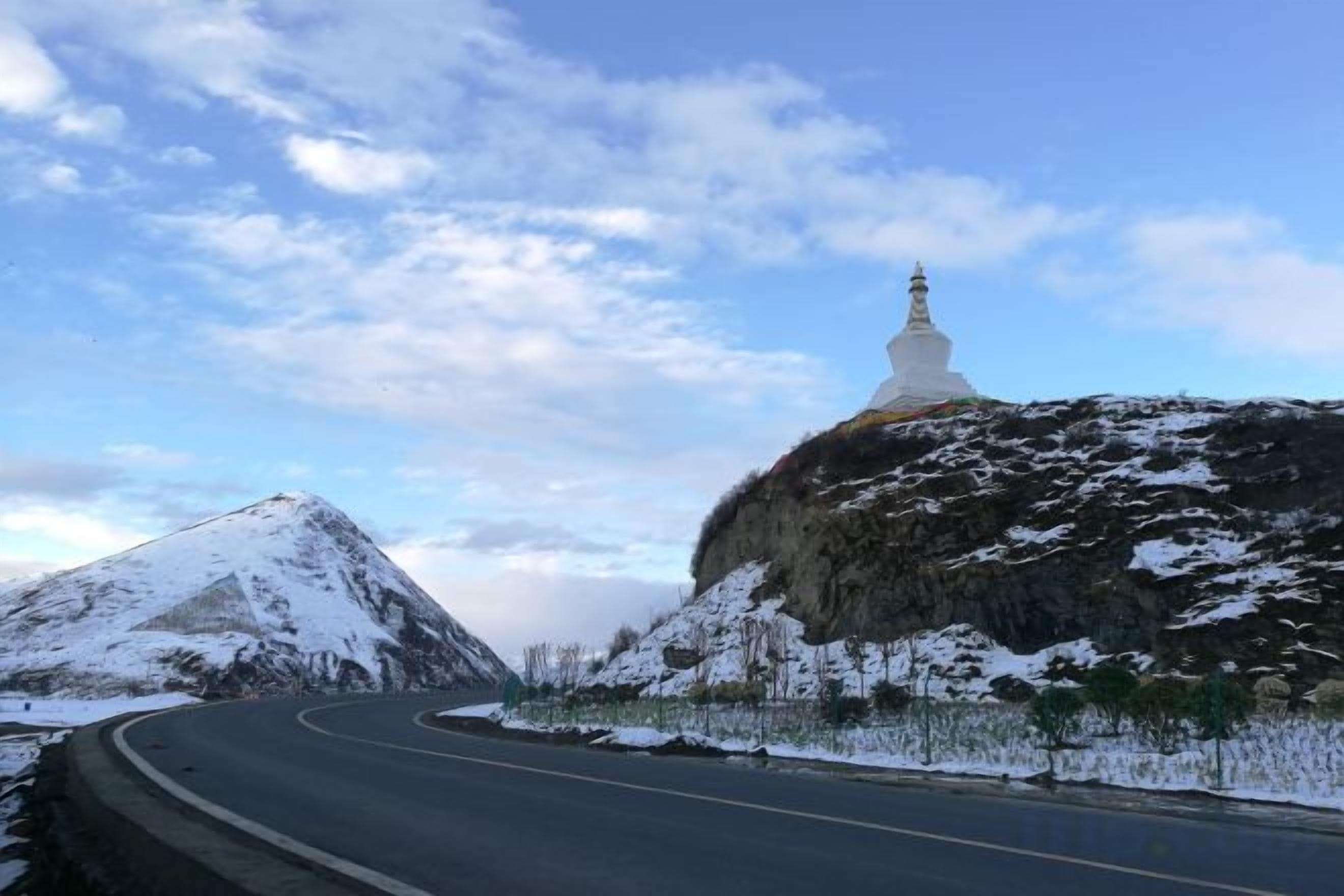A winding road with a snow-covered mountain and a white building on top.