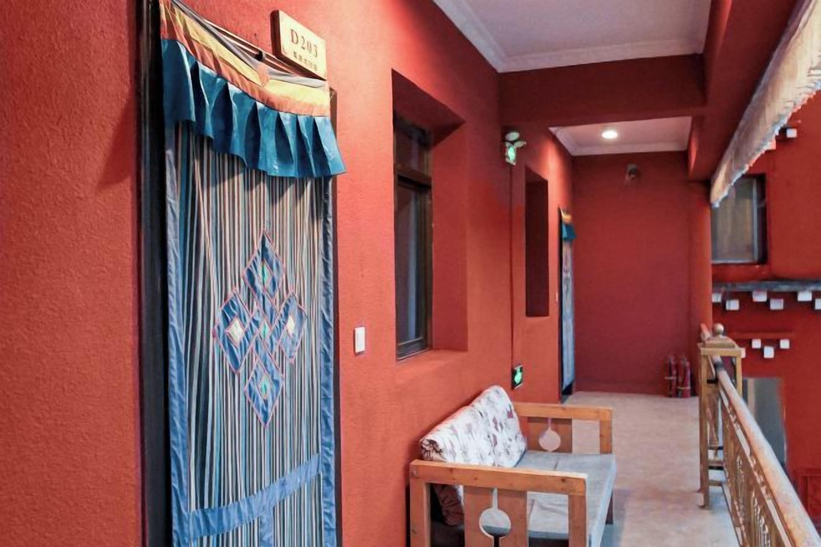 A corridor with a red wall, a wooden bench, and a door with a sign.