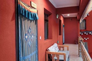 A corridor with a red wall, a wooden bench, and a door with a sign. - Garze Tagong Grassland Hotel (Kangding)