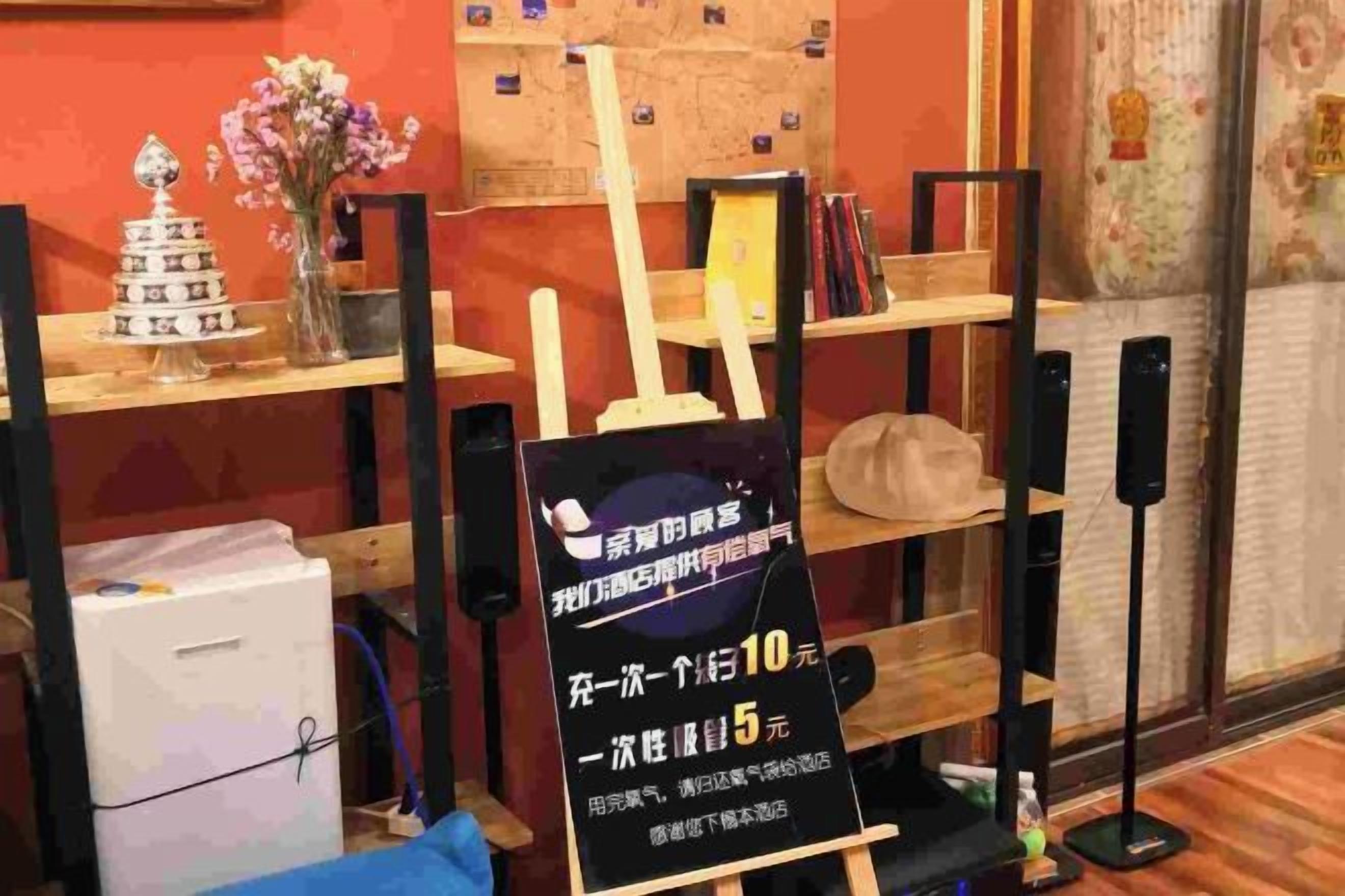 A room with a wooden shelf displaying various items, a sign with text, and a small table with a vase.