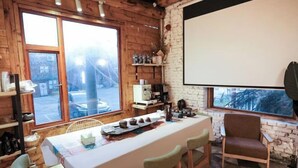 Una habitación acogedora con una mesa grande, sillas, una pantalla de proyector y un ventanal con vistas al exterior.