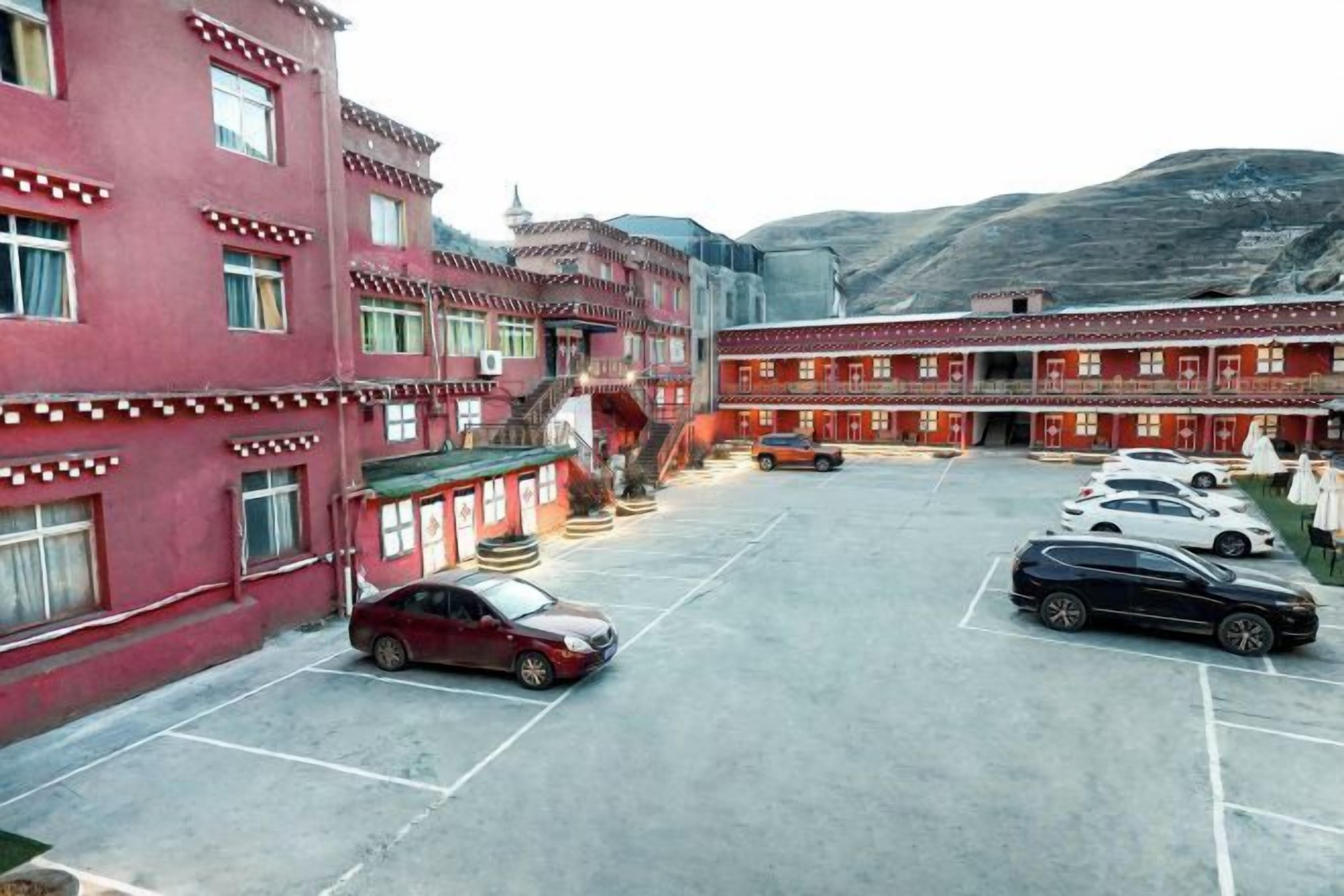A hotel with multiple floors, a parking lot with several cars, and a mountainous backdrop.