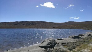 Una vista despejada de un lago con orilla rocosa y colinas a lo lejos.
