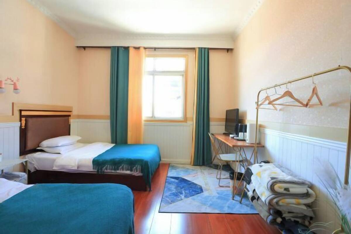 A hotel room with two beds, a desk with a chair, a TV, and a window with curtains.