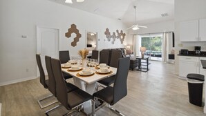 A modern dining area with a white table set for six, surrounded by dark chairs. A ceiling fan and pendant lights are visible above. - Great Community, amazing private pool, near Disney! (Davenport)