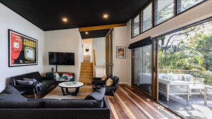 Un salon moderne doté d’un grand téléviseur, de sièges confortables et offrant une vue sur l’extérieur.