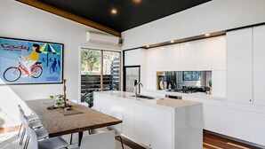 Une cuisine moderne avec des meubles blancs, un îlot central doté d’un évier et un coin repas avec une table en bois et des chaises blanches.