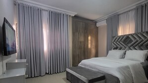 A modern bedroom with a large bed, a TV, and a wardrobe. - 4mins to Aso Rock Villa, King Bed, Chef, Free Cleaning, 24/7 Electricity, Games (Abuja)