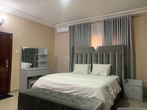 A bedroom with a large bed, a nightstand, a dresser, a mirror, and a window with curtains.