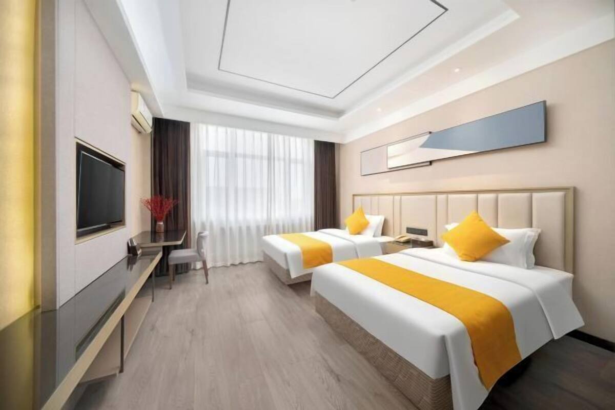 Une chambre d’hôtel avec deux lits, une télévision, un bureau et une grande fenêtre.