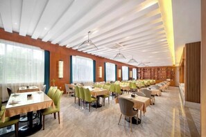 A spacious dining area with multiple tables and chairs, large windows, and a modern ceiling design.