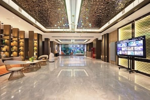 A spacious lobby with a high ceiling, a large digital display, and a seating area.