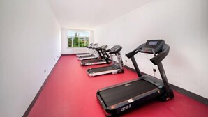 Un gimnasio con cintas de correr a lo largo de la pared, alfombra roja y una ventana con vistas al verdor.