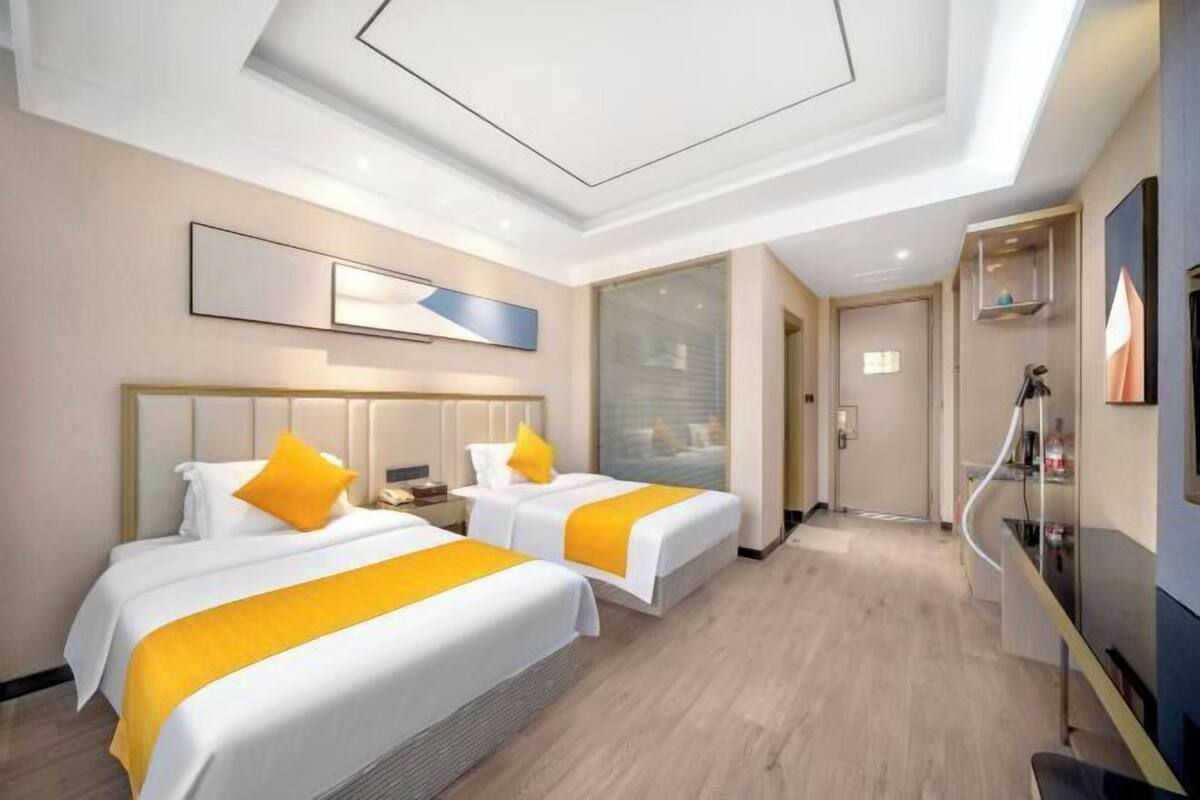 Une chambre d’hôtel avec deux lits, un design moderne au niveau du plafond et une salle de bain visible.