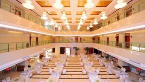 A spacious indoor area with multiple round tables and chairs, a high ceiling with hanging lights, and a glass railing on the upper level. - Yijiang Hotel (Wusu)