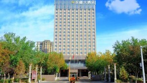 A tall hotel building with a modern facade, surrounded by trees and a clear sky. - Yijiang Hotel (Wusu)