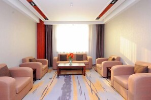A modern living room with sofas arranged around a central coffee table, a large window with curtains, and a patterned carpet. - Yijiang Hotel (Wusu)