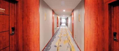 A hotel corridor with wooden walls and doors, a patterned carpet, and a straight path leading to the end.
