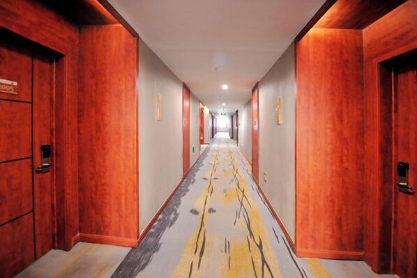 A hotel corridor with wooden walls and doors, a patterned carpet, and a straight path leading to the end.