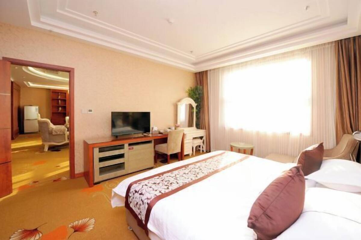 A hotel room with a bed, a desk, a television, a chair, a small table, and a mirror.