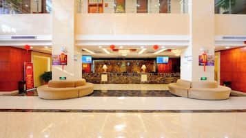 Un hall d’hôtel comprenant un comptoir d’accueil, un espace salon et un plafond haut orné d’un éclairage décoratif.