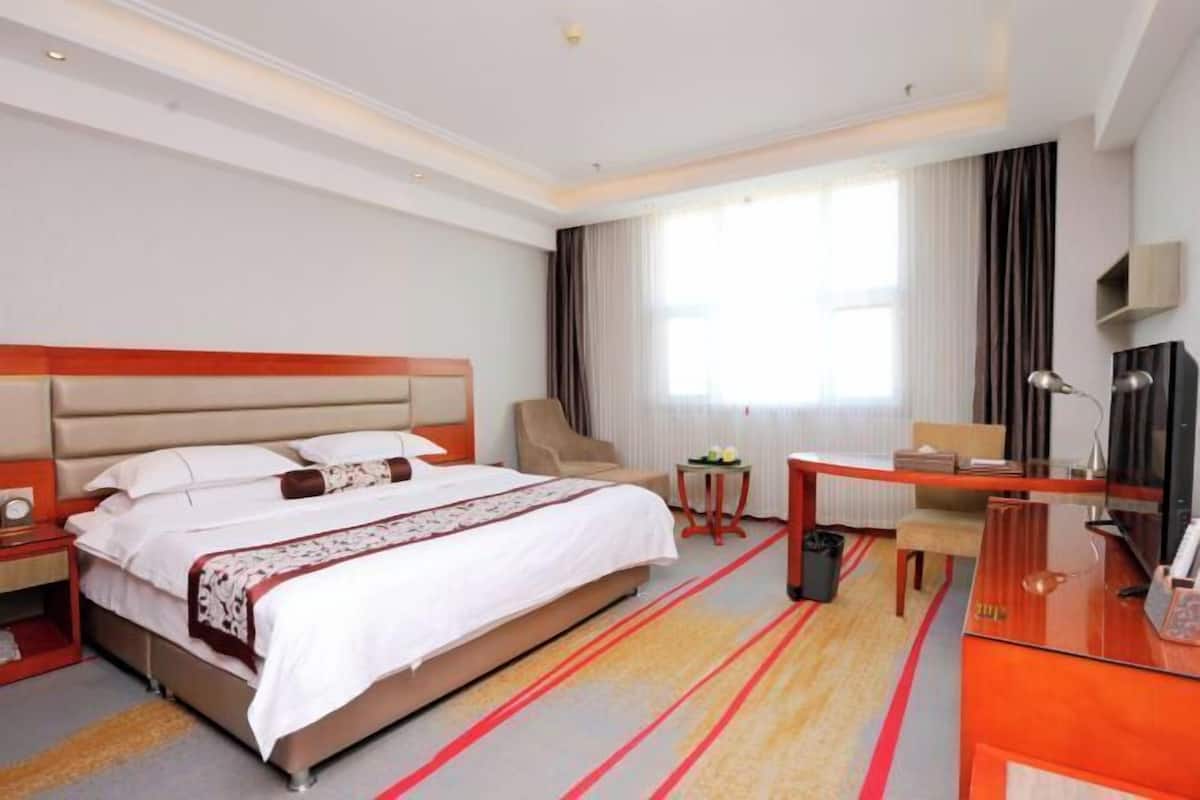 A hotel room with a bed, a desk, a chair, a TV, and a window with curtains.
