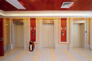Een hotellobby met vier liften, een receptiebalie en een marmeren vloer.