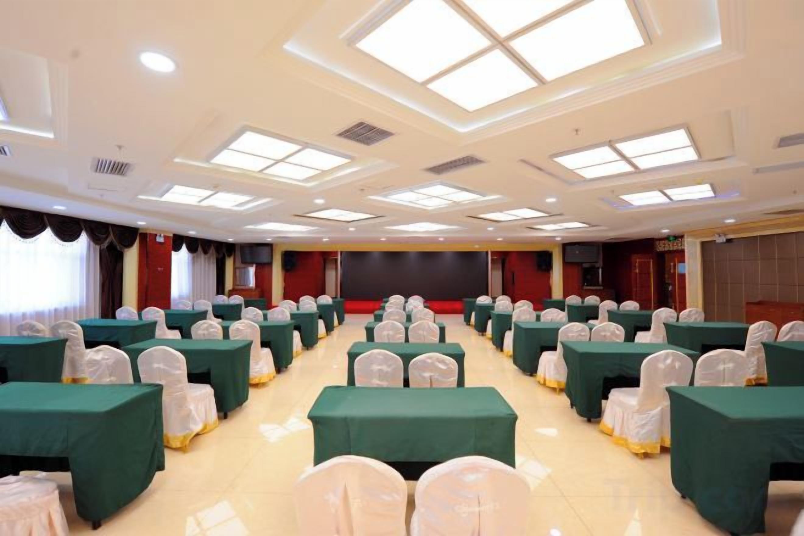 Une salle de conférence avec des rangées de tables et de chaises, une scène et un écran de projection.