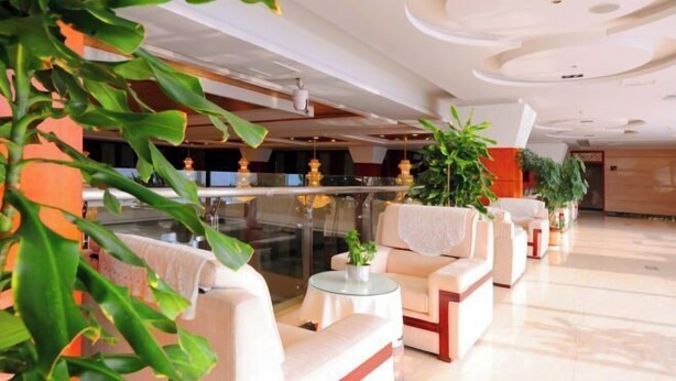 A modern hotel lobby with plush seating, a glass partition, and decorative plants. - Yijiang Hotel (Wusu)