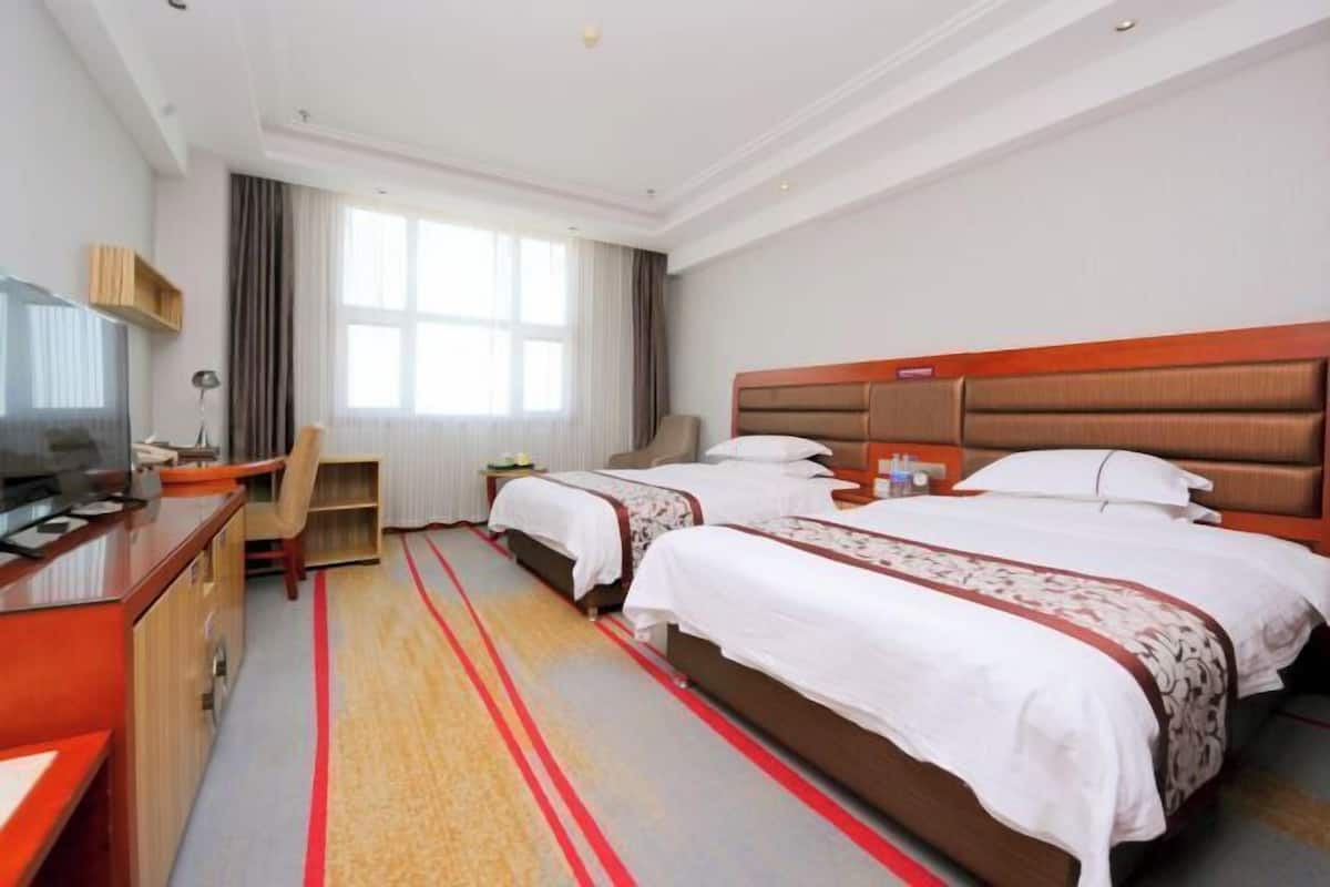 A hotel room with two beds, a desk, a TV, and a large window.