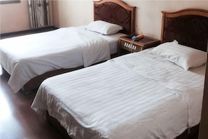 Two single beds with wooden headboards, white bedding, and a bedside table with a lamp. - Changning Xiuyuan Hotel (Changning)