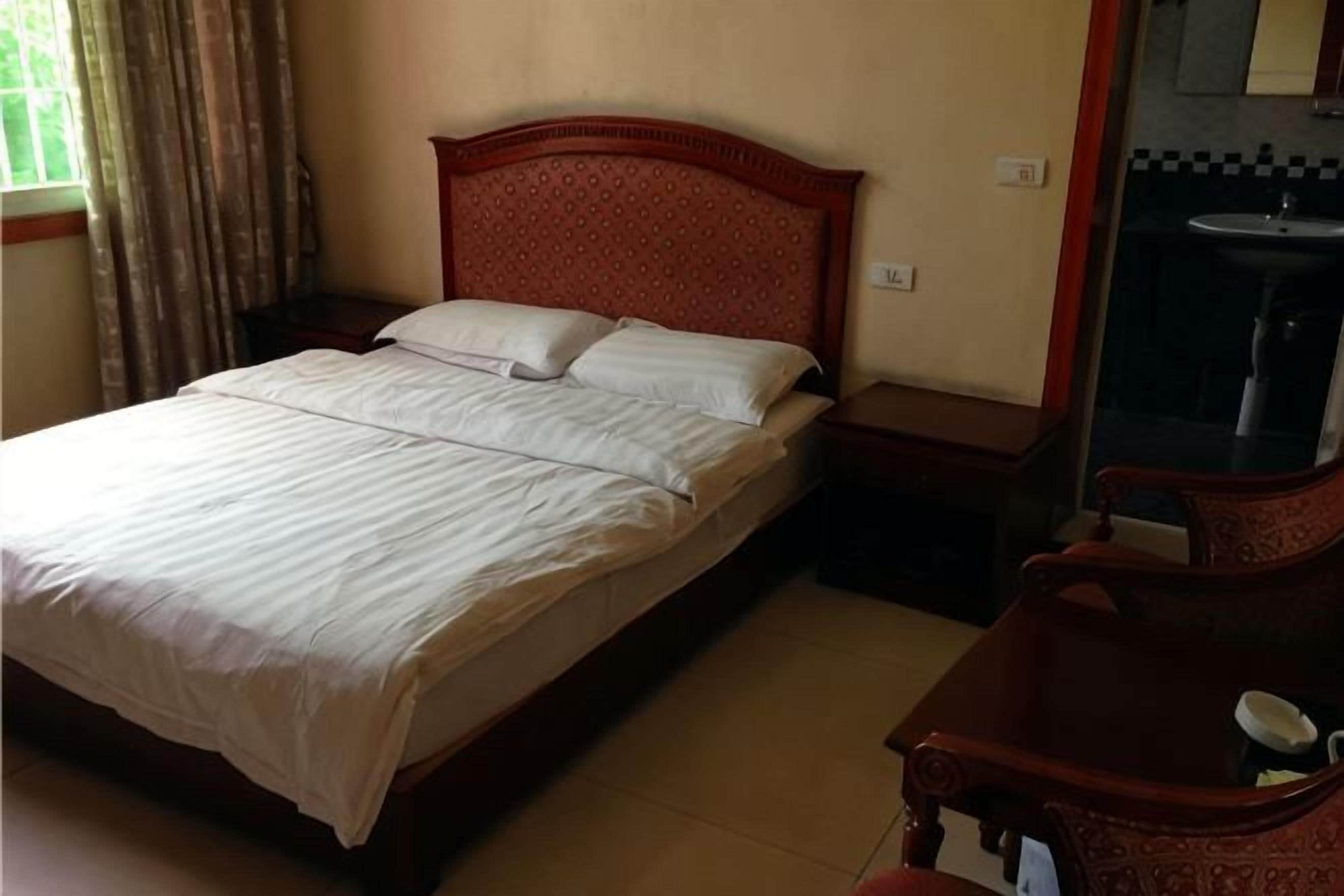 Una cama bien hecha con almohadas, un cabecero de madera, una mesita de noche con lámpara y un pequeño mueble de madera.