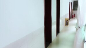 A narrow hallway with white walls and a tiled floor, leading to a room with a wooden door. - Changning Xiuyuan Hotel (Changning)