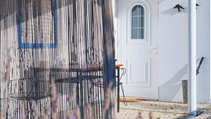 A building with a white exterior, a door, and a window. There is a blue awning and a fence with vertical slats. - Monte das Estrelas (Tavira)