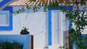 A white building with blue trim and shutters, a small garden with plants, and a tiled roof. - Monte das Estrelas (Tavira)
