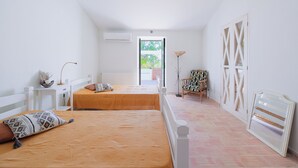 A bedroom with two beds, a radiator, a desk, a chair, and a view through a door. - Monte das Estrelas (Tavira)