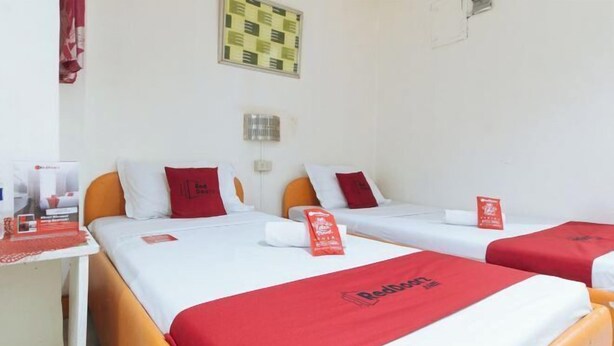 A hotel room with three beds, each with a red bedspread and matching pillows. There is a small table with a red tablecloth and a red sign on it. - RedDoorz @ Golden Travellers Inn Antique (San Jose de Buenavista)
