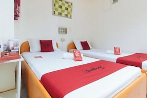 Una habitación de hotel con tres camas, cada una con una colcha roja y almohadas a juego. Hay una mesita con mantel rojo y una señal roja encima.