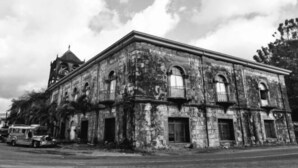 An old, weathered building with arched windows and a bell tower, surrounded by trees and parked vehicles. - RedDoorz @ Golden Travellers Inn Antique (San Jose de Buenavista)