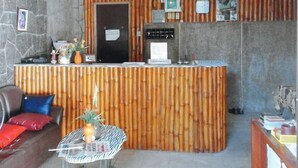A reception area with a bamboo panel wall, a reception desk, a computer, and a small table with a vase and a pineapple.