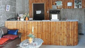A reception area with a bamboo panel backdrop, a reception desk, a coffee machine, and a small table with a newspaper. - RedDoorz @ Golden Travellers Inn Antique (San Jose de Buenavista)