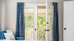 Een slaapkamer met een bed, een blauwe bank en een balkon met gordijnen met een patroon.
