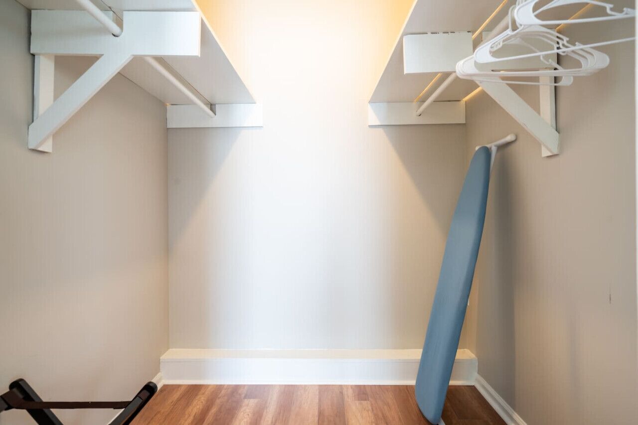Une pièce avec un plancher en bois, des murs blancs et une planche à repasser bleue appuyée contre le mur.