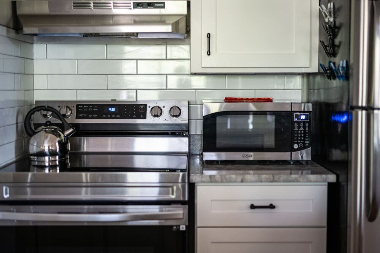 Una cucina con un piano cottura in acciaio inossidabile, un forno a microonde e un bollitore.